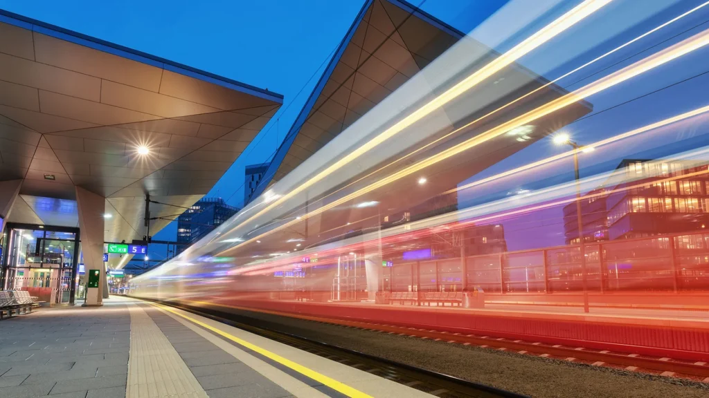 Ett tåg rusar förbi en perrong i en stad.