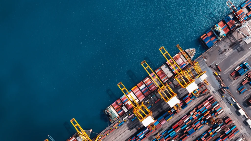 Ett lastfartyg lastas i en hamn. Bilden är tagen ovanifrån.