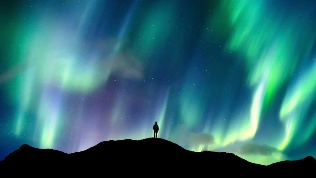 En person står på en kulle och tittar på ett spektakulärt norrsken.
