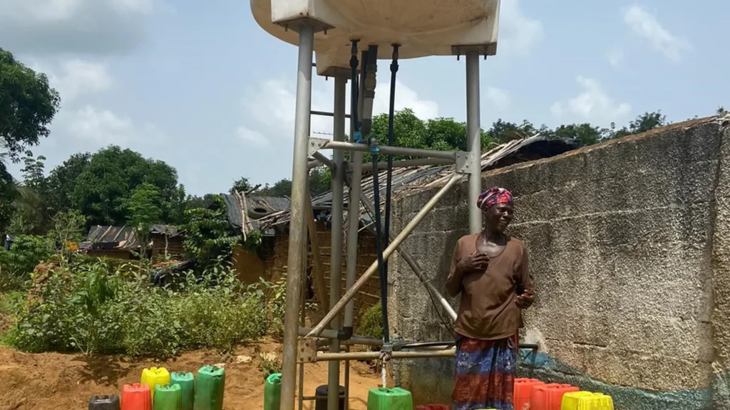 Bild från projektet water for all i Elfenbenskusten. På bilden syns ett mindre vattentorn. Vid foten av tornet står en kvinna och flera vattendunkar.