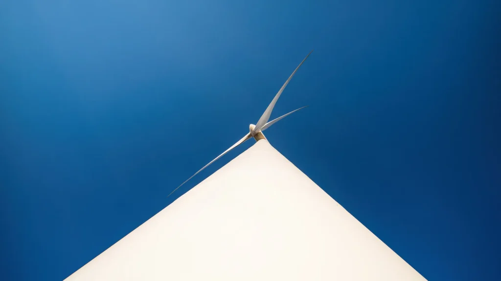 Ett vindkraftverk sett från botten av kraftverket. Himlen bakom är djupt blå.