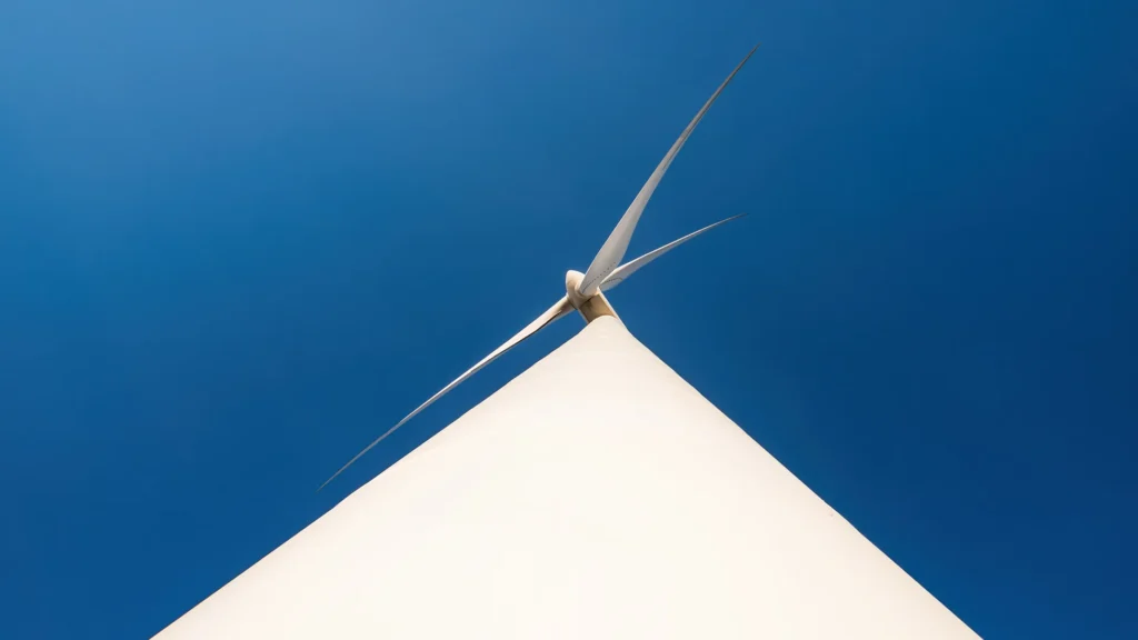 Ett vindkraftverk sett från botten av kraftverket. Himlen bakom är djupt blå.