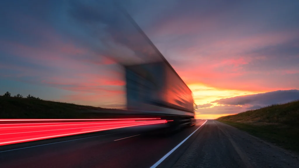 Lastbil som kör på en väg mot solnedgången.